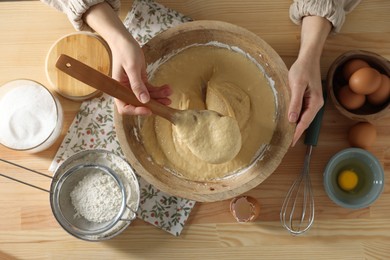 Photo of Woman kneading dough with spoon in bowl at wooden table, top view