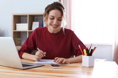 Photo of Young woman working with laptop at desk. Home office