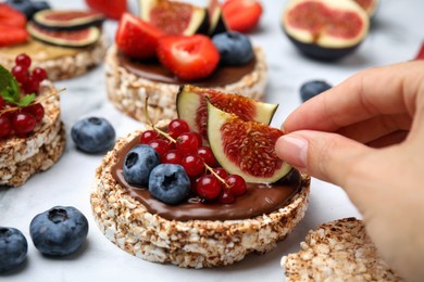 Photo of Woman decorating crispbreads with fig at table, closeup