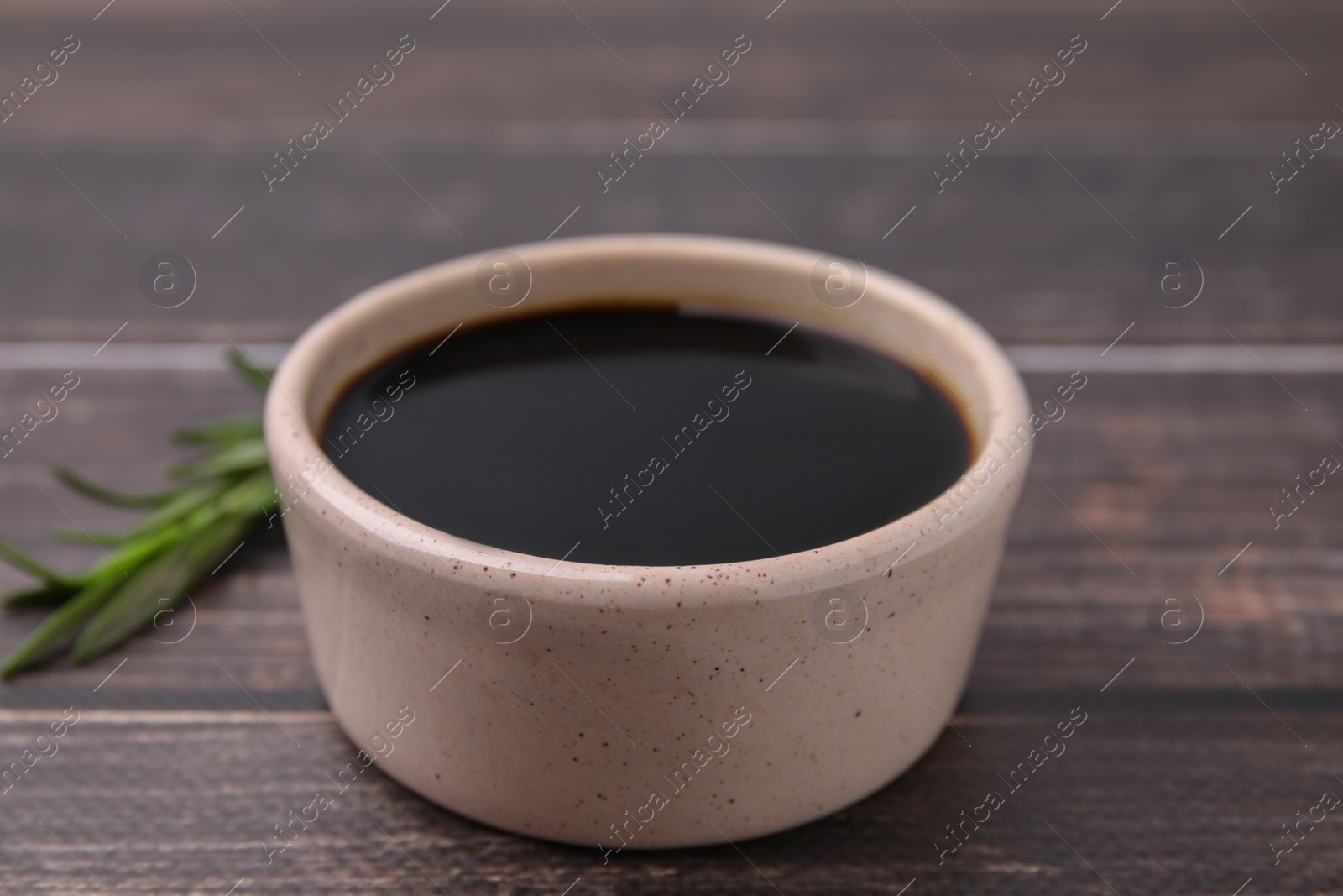 Photo of Bowl with balsamic vinegar on wooden table, closeup