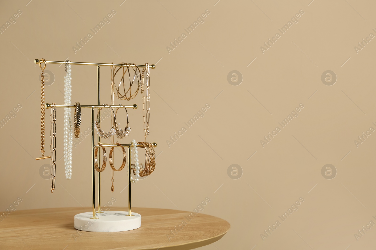 Photo of Holder with set of luxurious jewelry on wooden table near beige wall, space for text