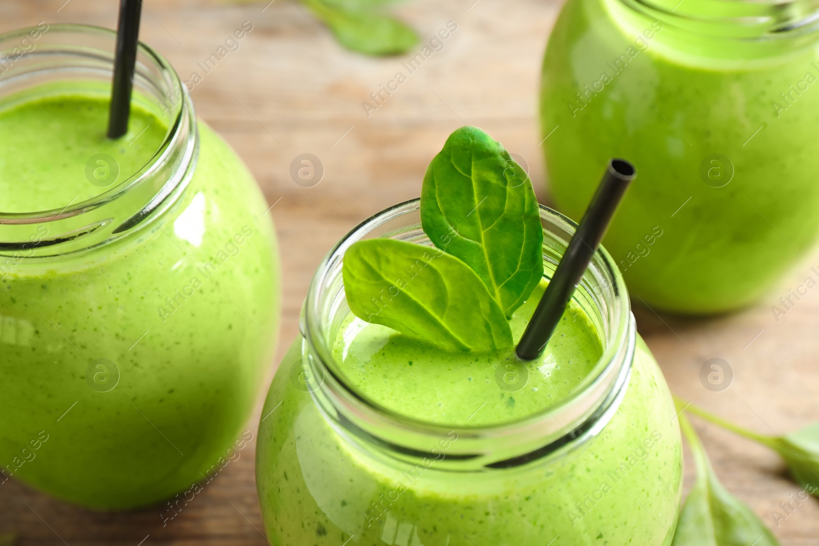 Photo of Jars of healthy green smoothie with fresh spinach on wooden table, closeup view