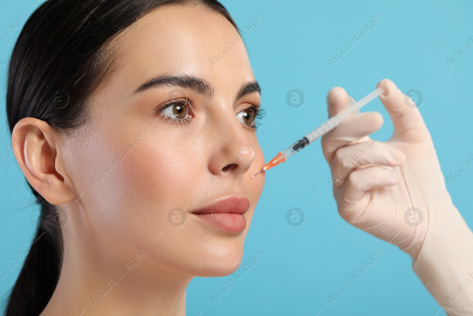 Photo of Doctor giving facial injection to young woman on light blue background, closeup. Cosmetic surgery