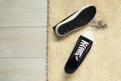 Photo of Black sneakers and mud on beige carpet, top view. Space for text