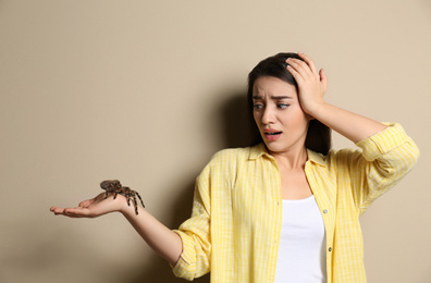 Photo of Scared young woman holding tarantula on beige background. Arachnophobia (fear of spiders)