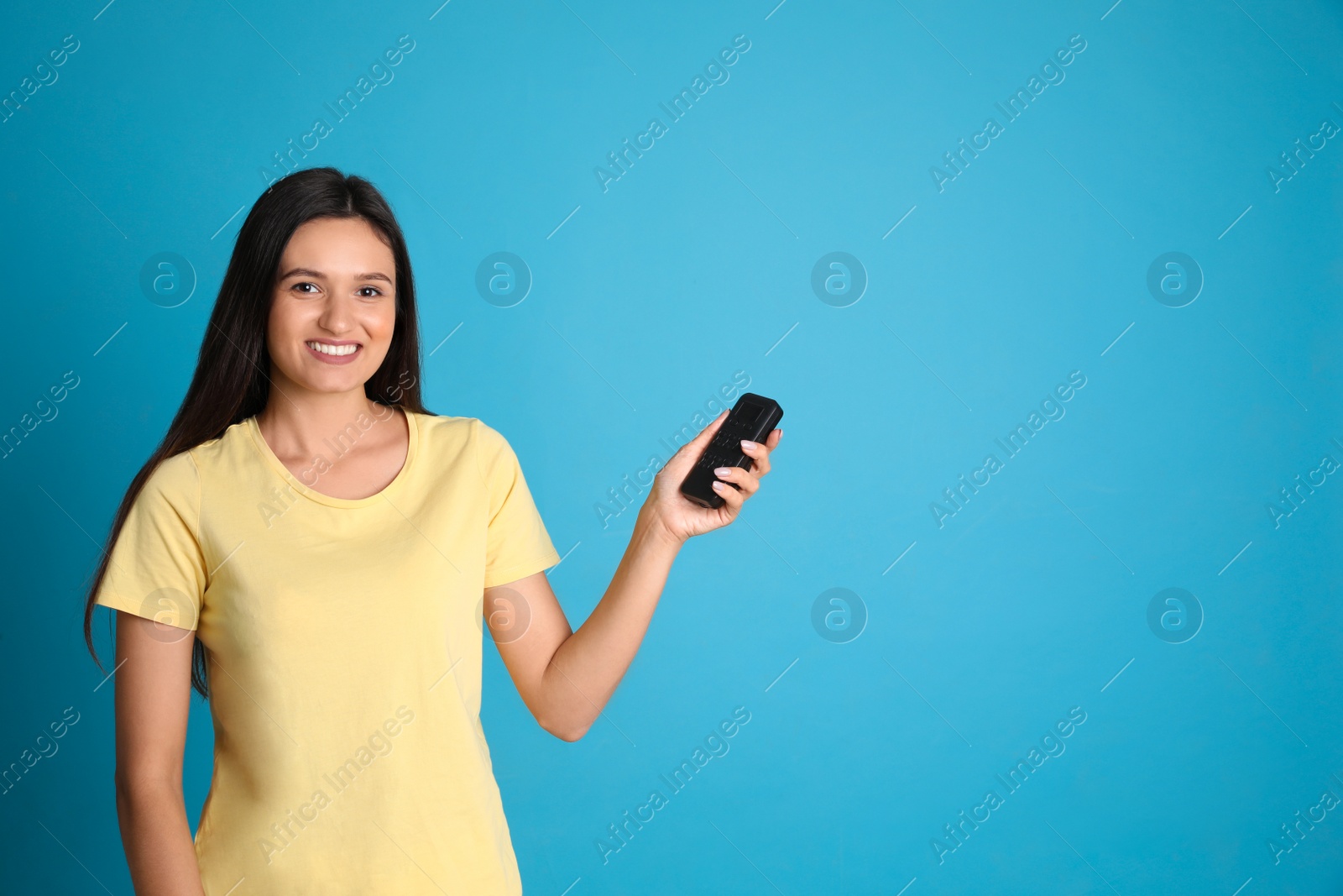 Photo of Happy young woman operating air conditioner with remote control on light blue background. Space for text