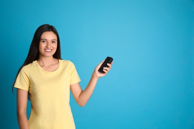 Photo of Happy young woman operating air conditioner with remote control on light blue background. Space for text