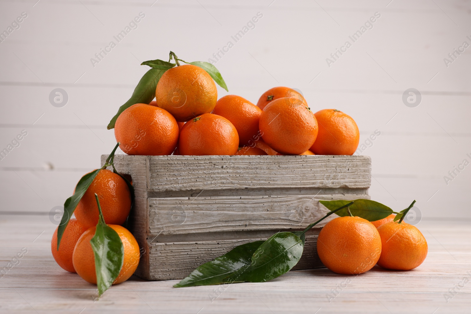 Photo of Delicious tangerines with leaves on light wooden table