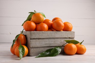 Delicious tangerines with leaves on light wooden table