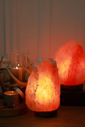 Photo of Himalayan salt lamps, candles and gemstones on wooden table near white wall indoors