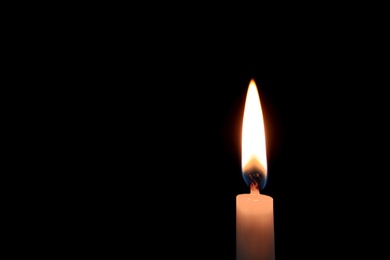 Photo of Wax candle burning on black background