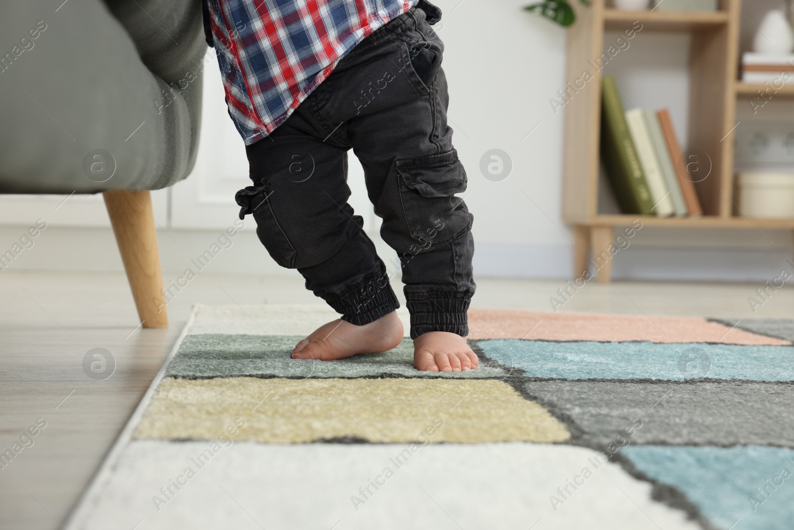 Photo of Baby standing on soft carpet near sofa, closeup. Space for text