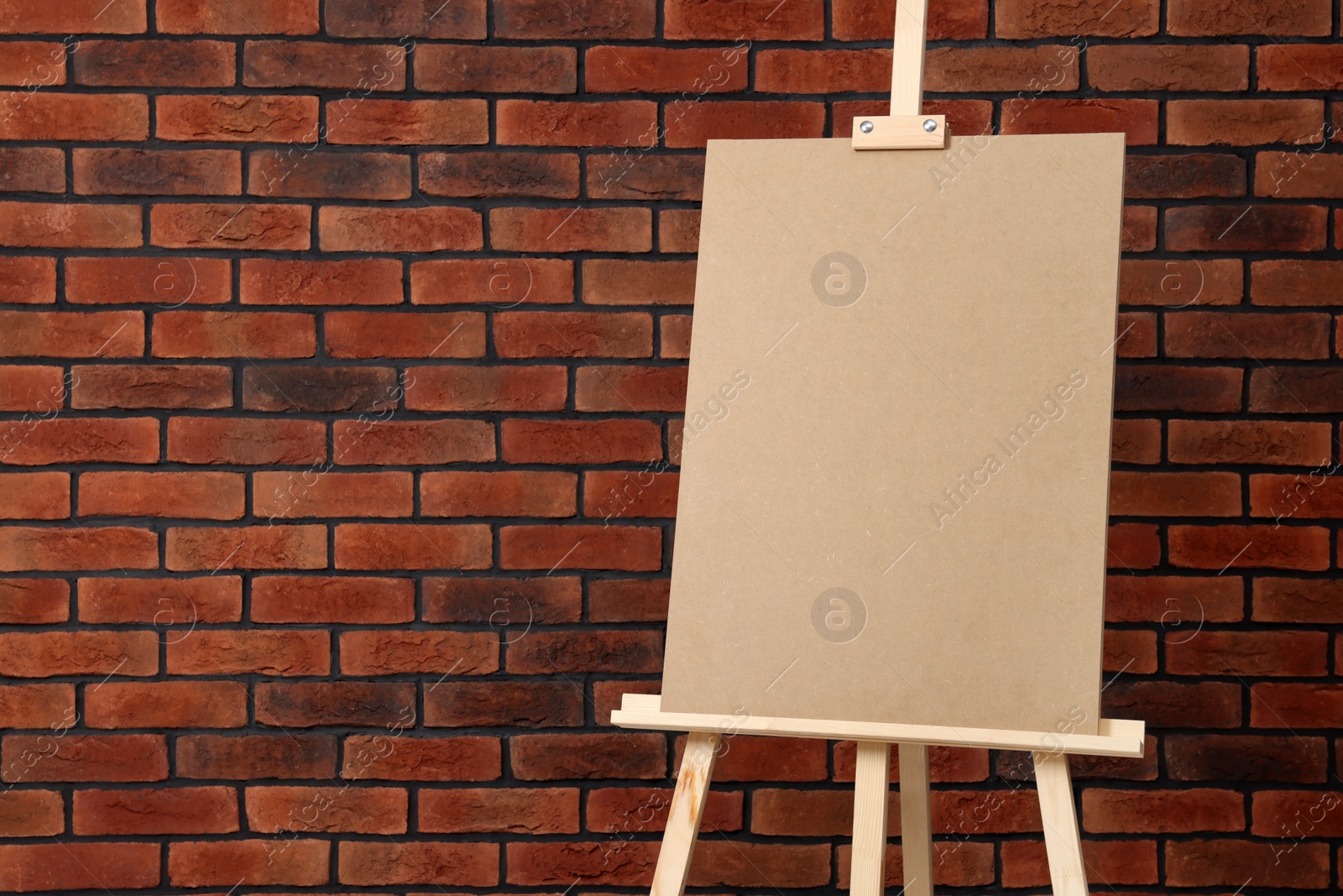 Photo of Wooden easel with blank board near brick wall, closeup. Space for text
