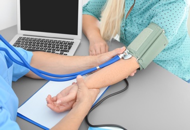 Close up view of medical assistant measuring female patient blood pressure in clinic