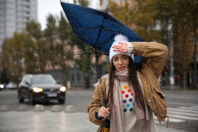 Photo of Woman with blue umbrella caught in gust of wind on street