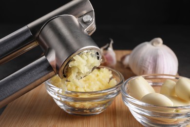 Photo of Crushing garlic with press into bowl at wooden table, closeup