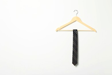 Photo of Hanger with striped necktie on white wall. Space for text