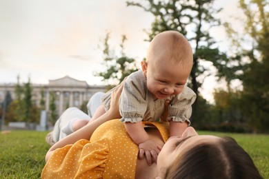 Happy mother with adorable baby lying on green grass in park