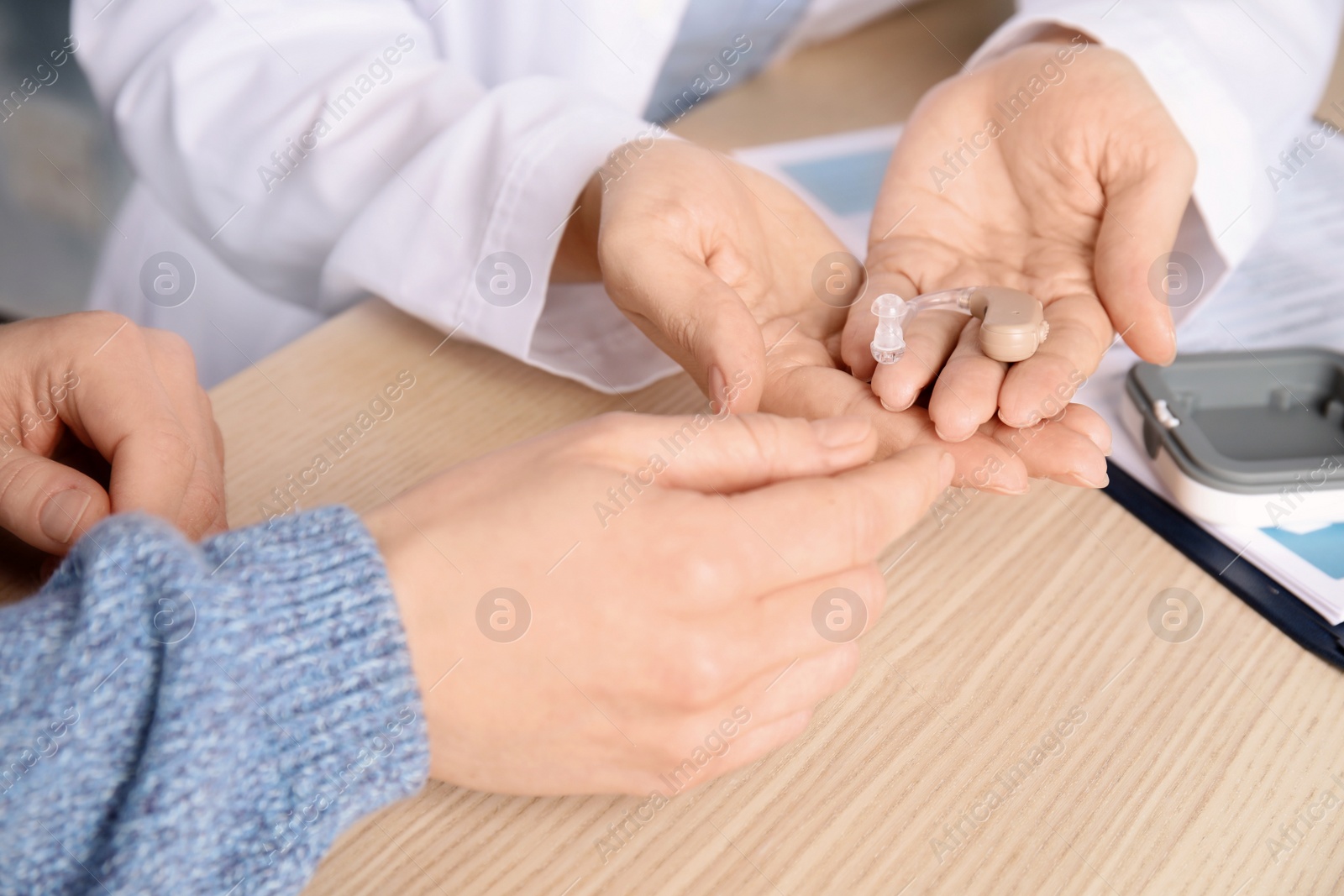 Photo of Doctor giving patient hearing aid at table in clinic, closeup