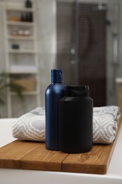 Wooden bath tray with bottles of shower gels and towel on tub indoors, space for text