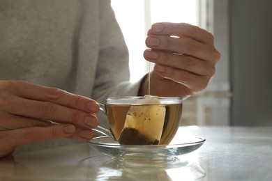 Photo of Woman taking tea bag out of cup at table indoors, closeup