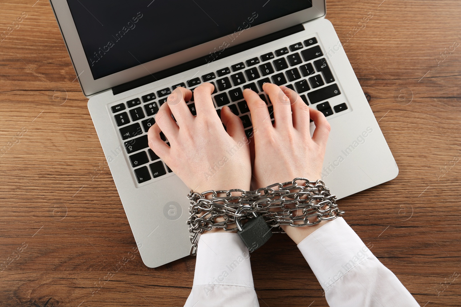Photo of Woman with chained hands typing on laptop at wooden table, top view. Internet addiction