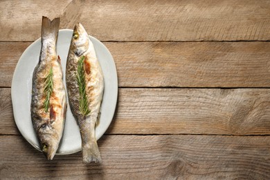 Photo of Delicious baked fish and rosemary on wooden table, top view. Space for text