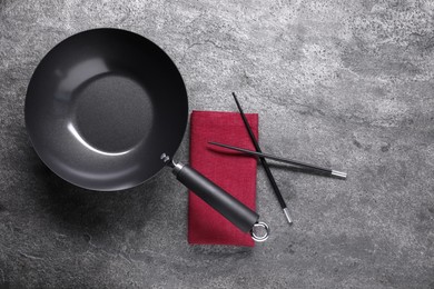 Photo of Empty iron wok and chopsticks on grey table, flat lay