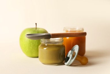 Photo of Healthy baby food, apple, pacifier and spoon on beige background