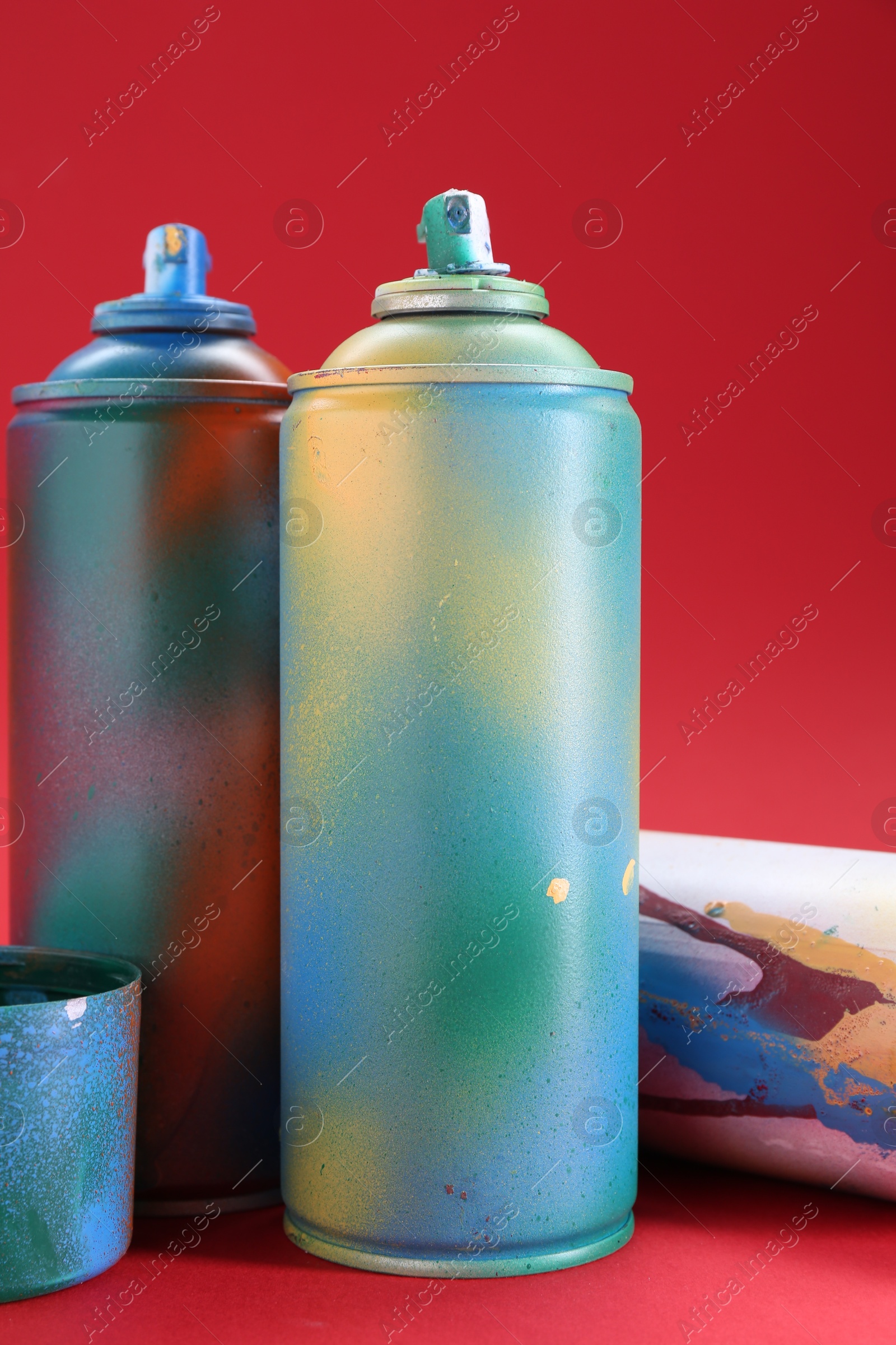 Photo of Bright spray paint cans on red background, closeup