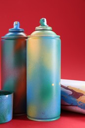 Photo of Bright spray paint cans on red background, closeup