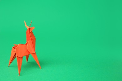 Photo of Origami art. Handmade orange paper deer on green background, space for text