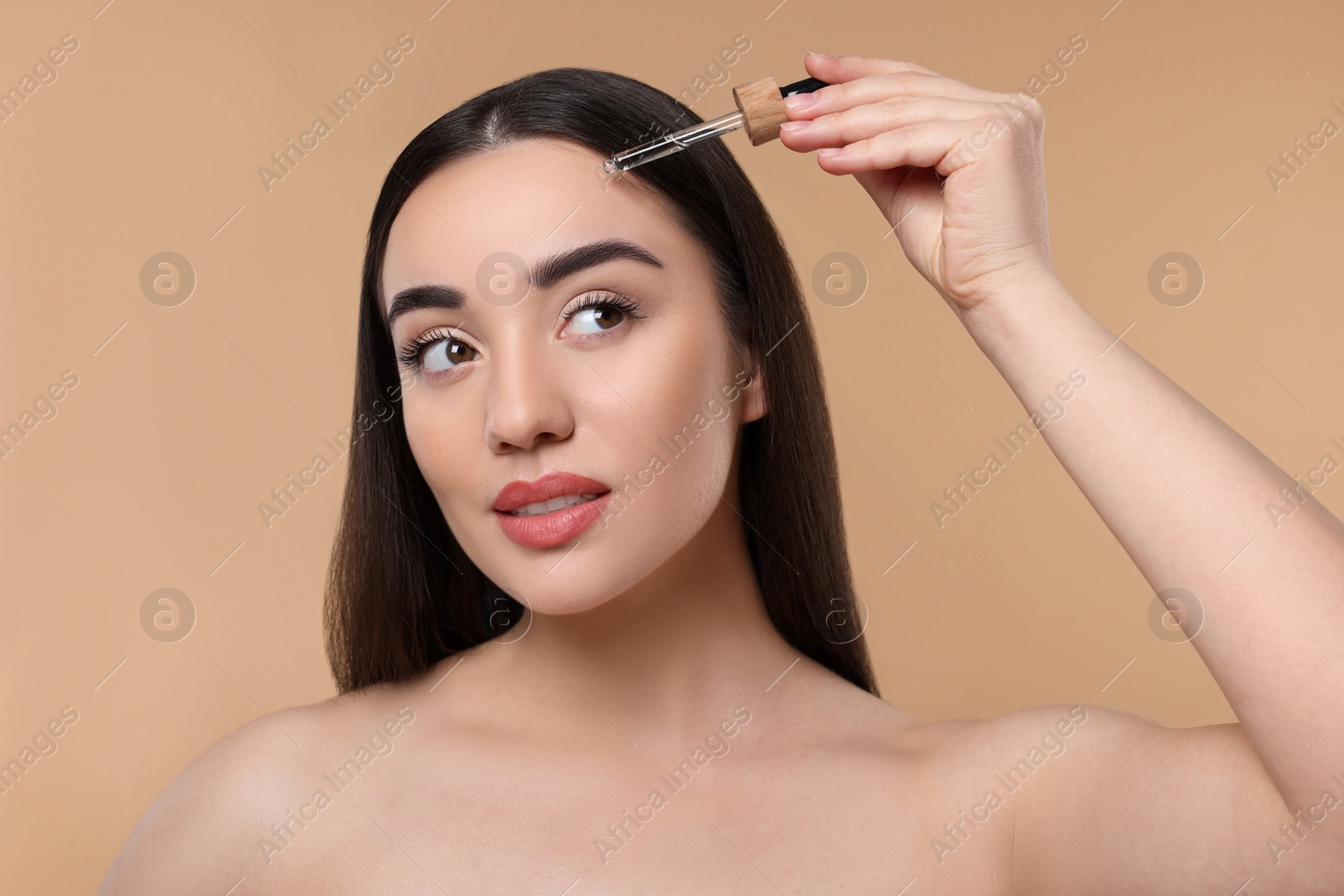 Photo of Young woman applying essential oil onto face on beige background