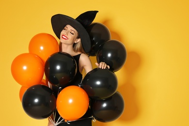 Photo of Beautiful woman wearing witch costume with balloons for Halloween party on yellow background, space for text