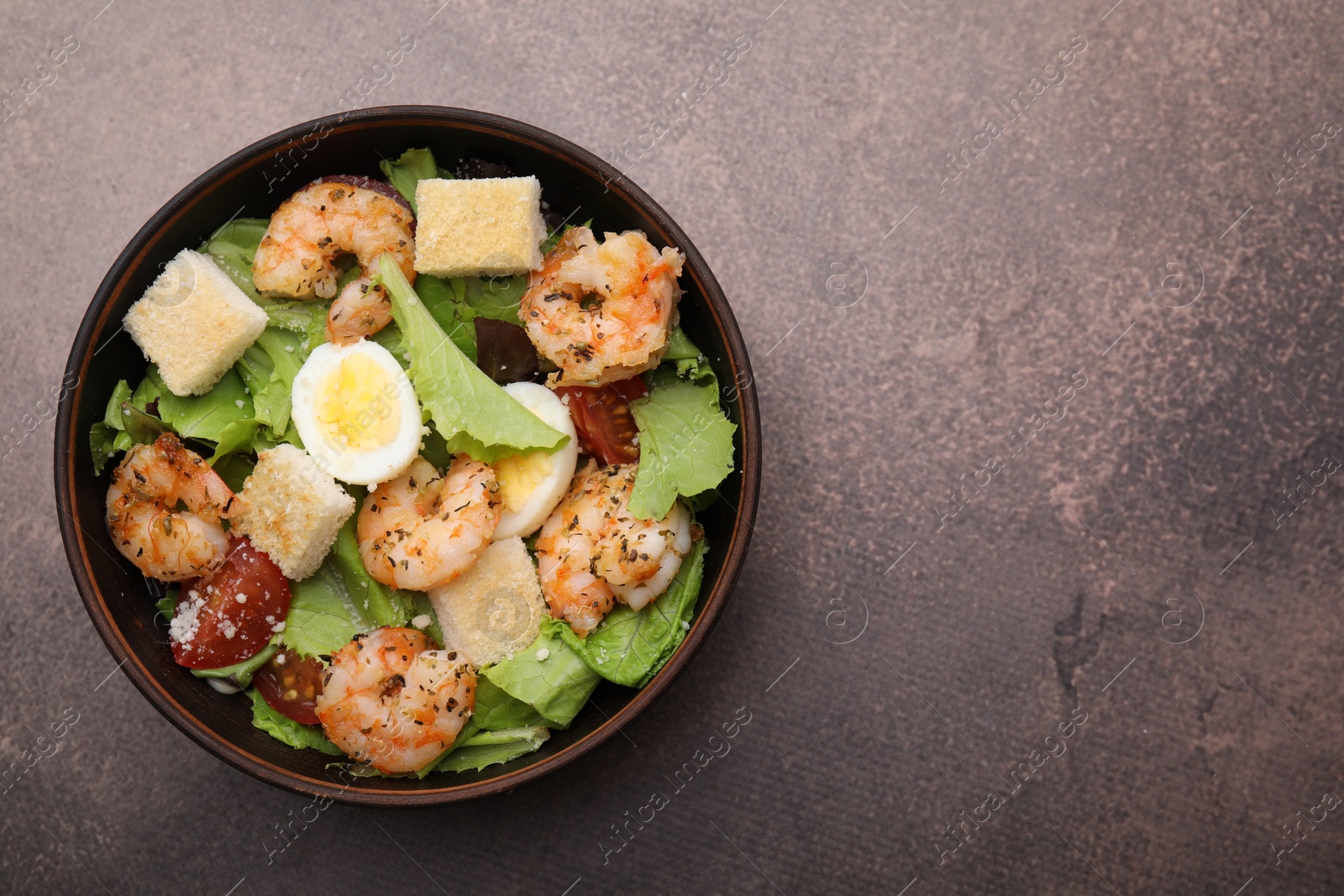 Photo of Delicious Caesar salad with shrimps on brown table, top view. Space for text