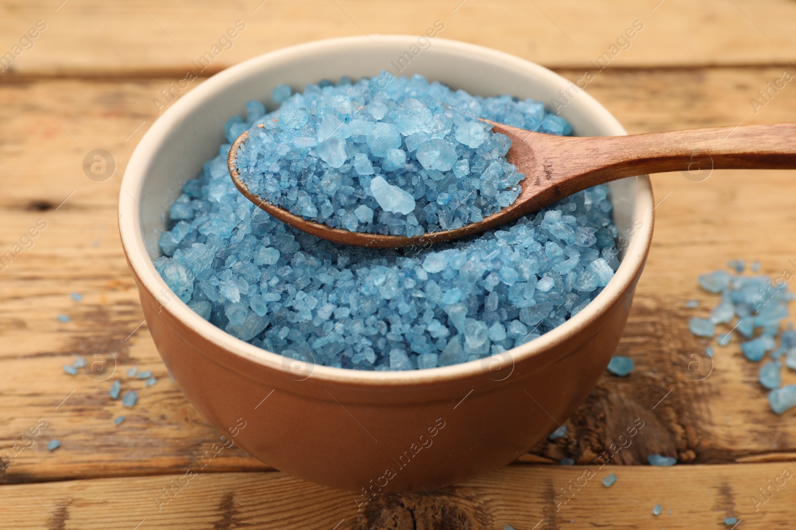 Photo of Bowl and spoon with blue sea salt on wooden table, closeup