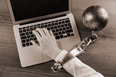 Image of Top view of woman with ball and chain on her hand using laptop at wooden table, sepia effect. Internet addiction