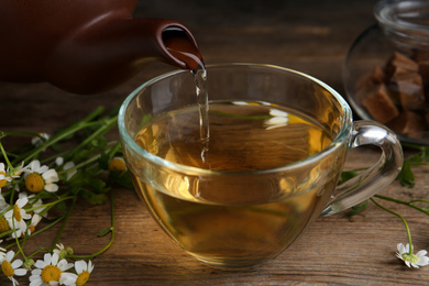 Pouring tasty chamomile tea into glass cup on wooden table