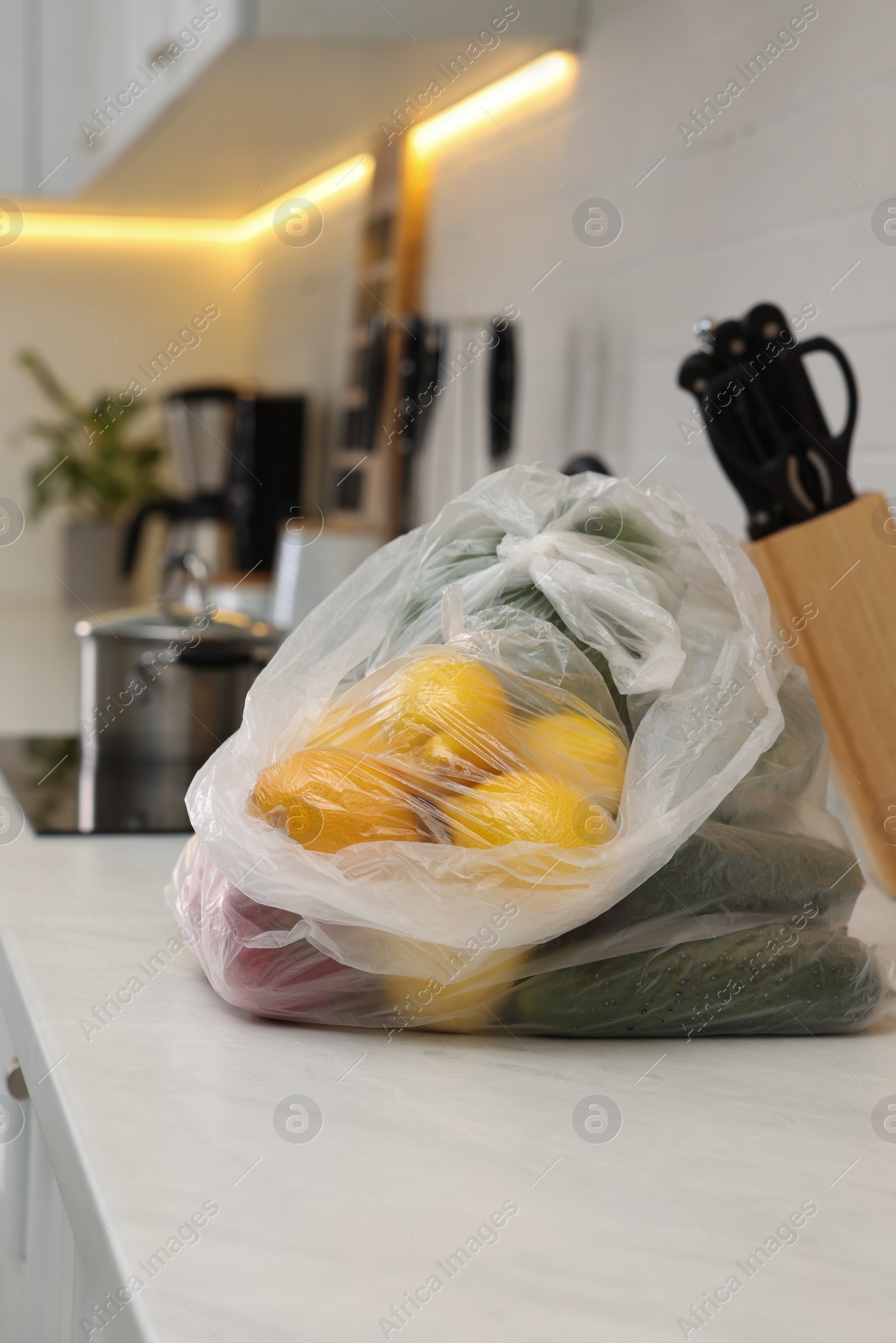Photo of Plastic bags with different fresh products on white countertop in kitchen