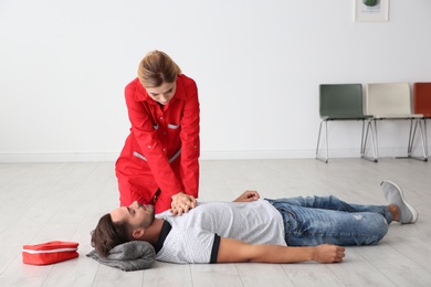 Photo of Woman in uniform practicing first aid on unconscious man indoors