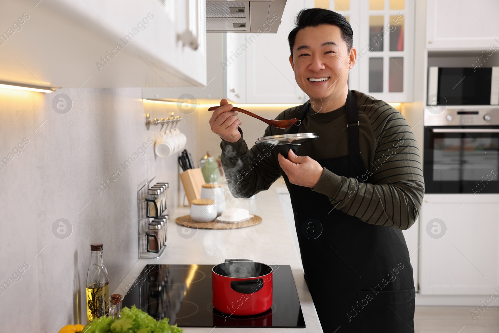 Photo of Cooking process. Happy man tasting dish in kitchen