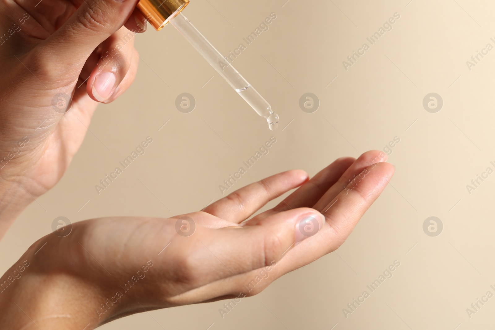 Photo of Woman applying cosmetic serum onto her finger on beige background, closeup