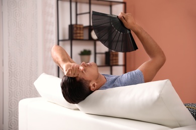 Man with hand fan on sofa. Summer season