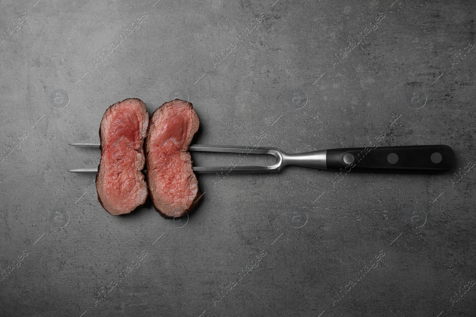 Photo of Fork with slices of meat on grey table, top view