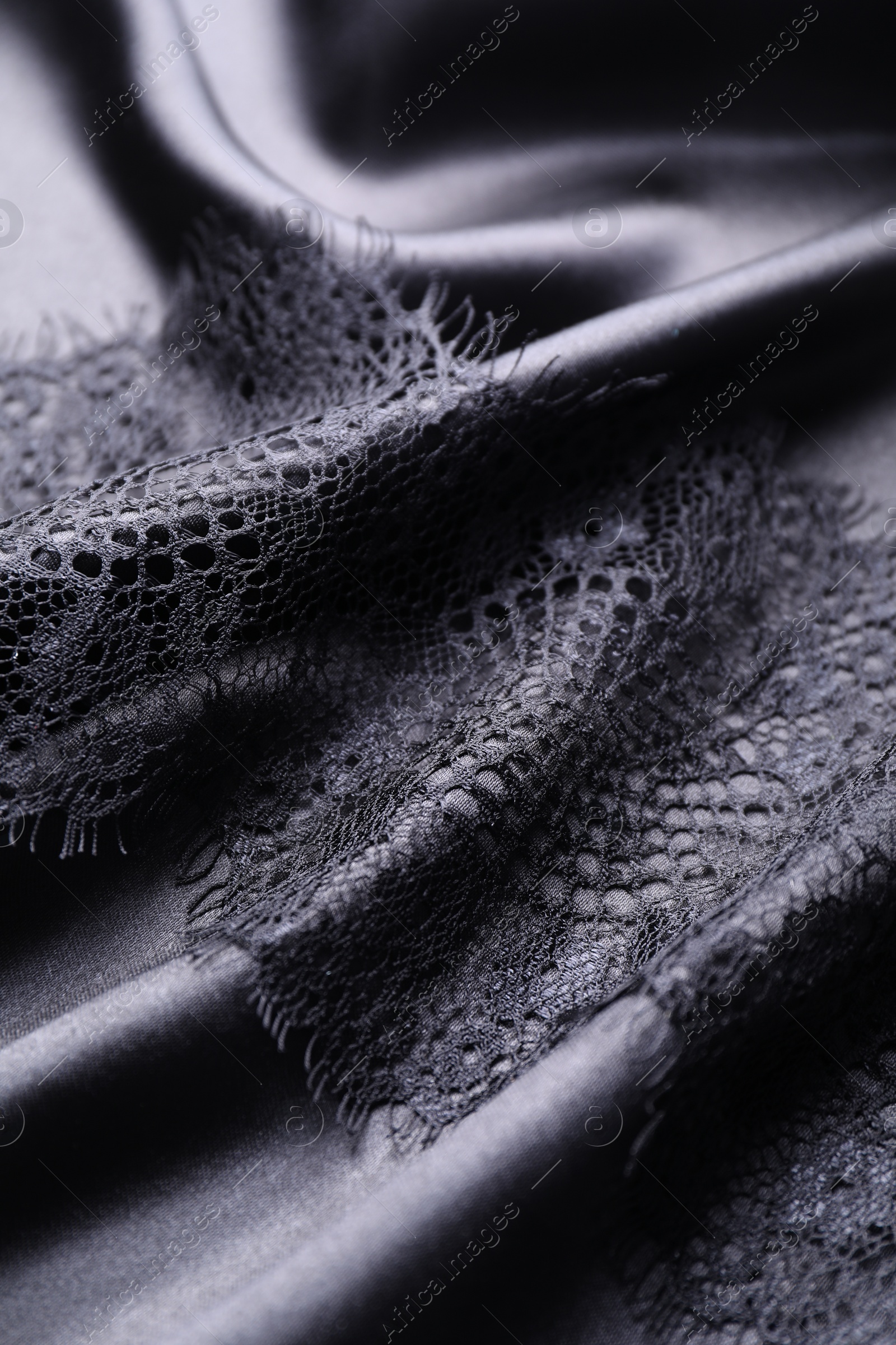 Photo of Beautiful lace with pattern on black fabric, closeup