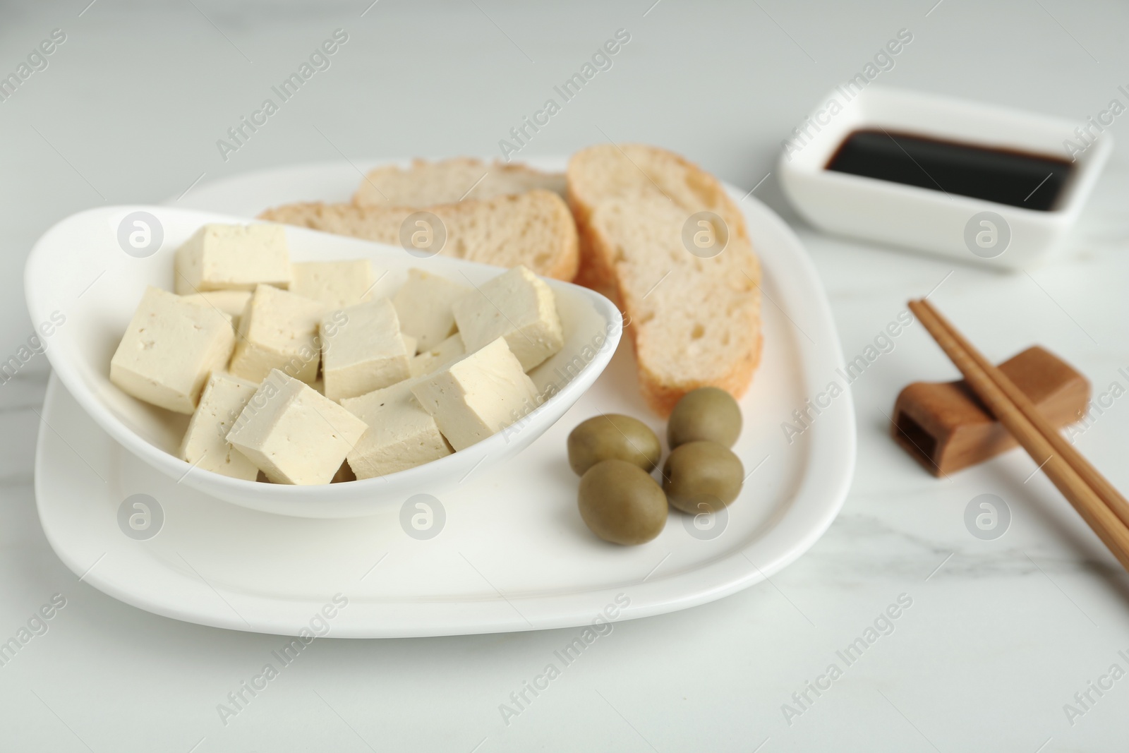 Photo of Pieces of delicious tofu with olives and bread served on white marble table