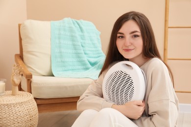 Photo of Young woman with modern electric fan heater at home