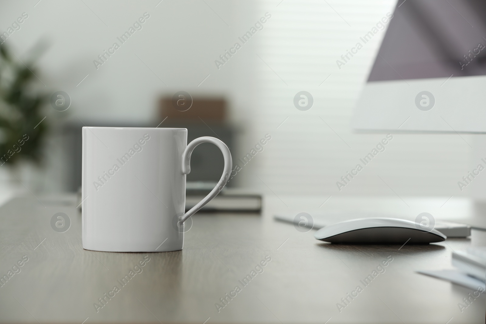 Photo of White ceramic mug on wooden table at workplace. Mockup for design