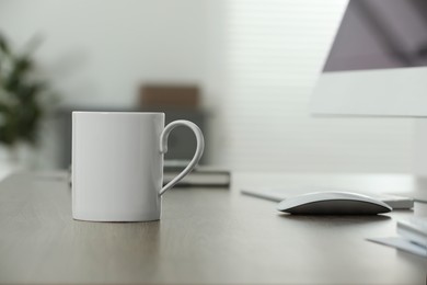 Photo of White ceramic mug on wooden table at workplace. Mockup for design