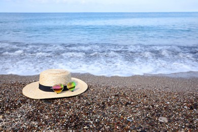 Photo of Straw hat and colorful heart shaped sunglasses on sea beach. Space for text